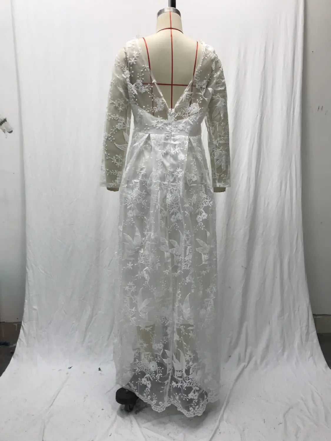 A delicate white lace off shoulder long sleeve bridal wedding gown with intricate floral embroidery scalloped hem shown from the back with a deep v-back.