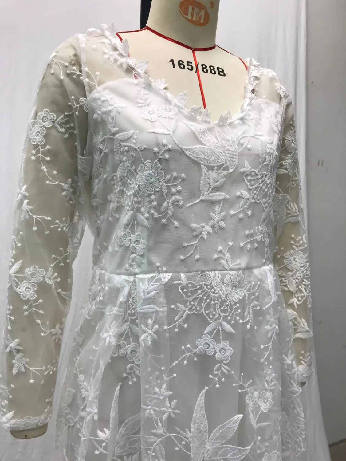 A delicate white off shoulder lace bridal wedding gown with intricate floral embroidery and long sheer sleeves displayed on a mannequin.