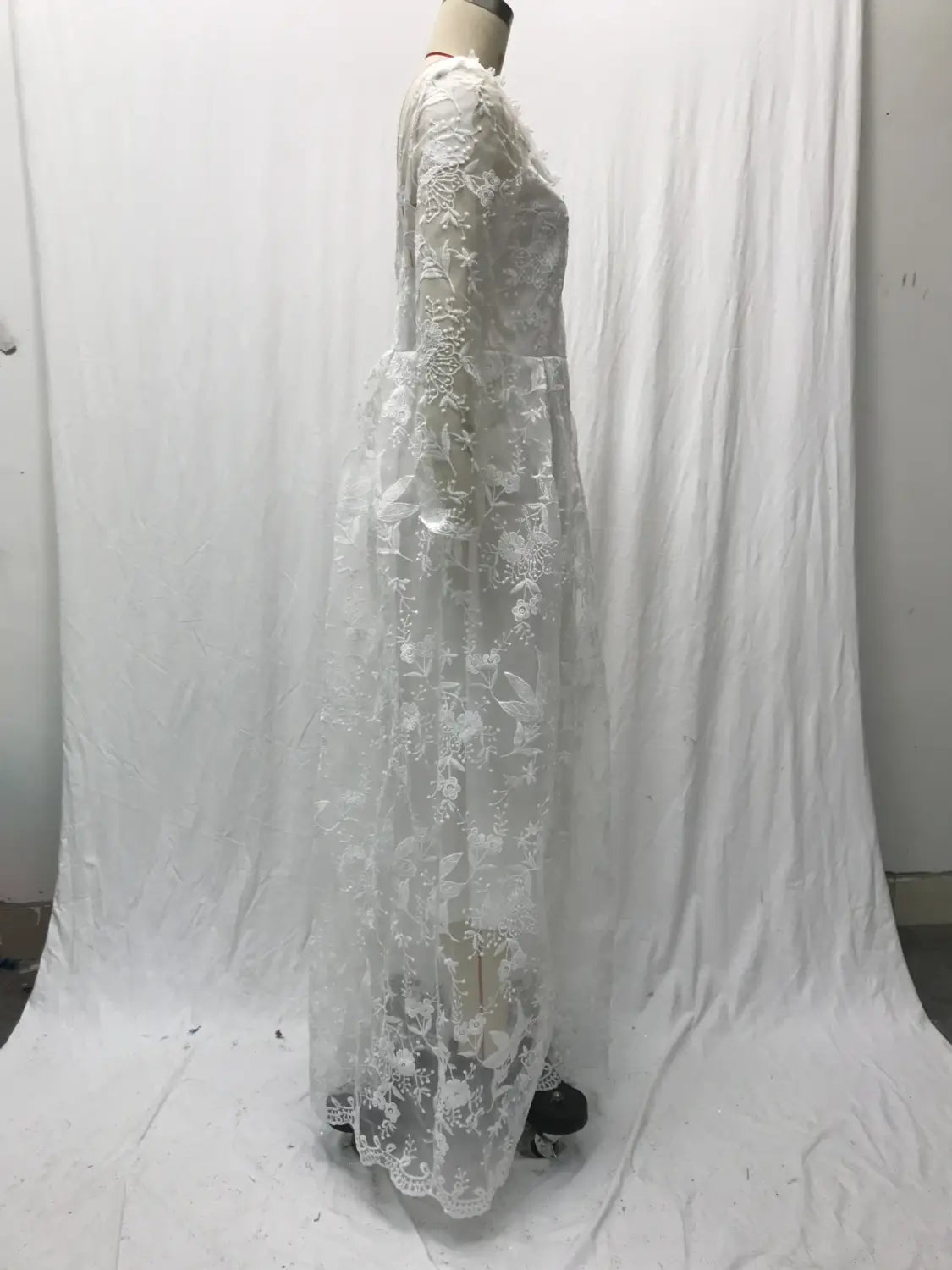 A flowing white lace off shoulder long sleeve bridal wedding gown with intricate floral embroidery displayed on a mannequin.