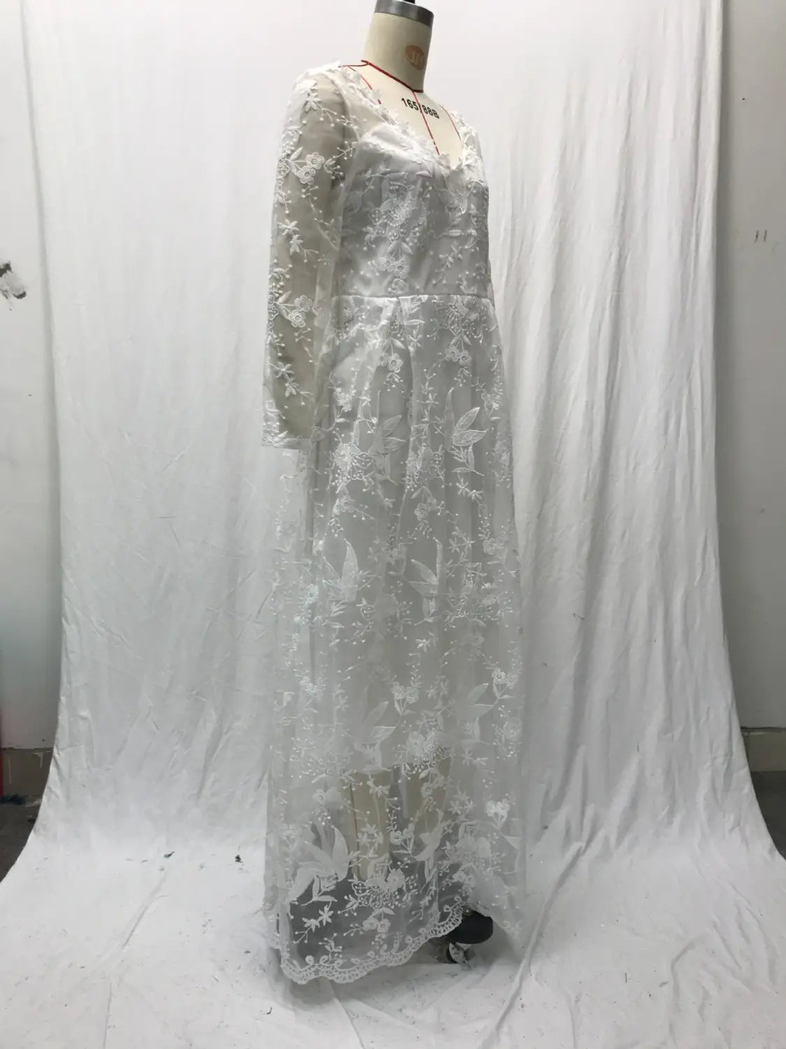 A delicate white lace off shoulder bridal wedding gown with intricate floral embroidery and long sleeves displayed on a mannequin.