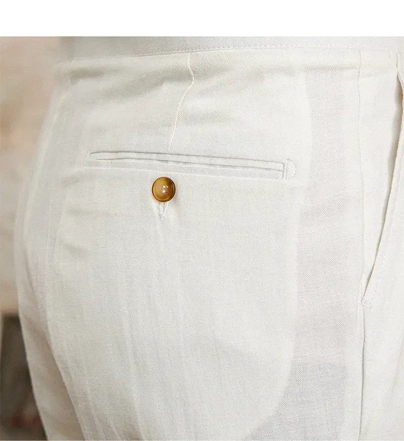 Pantalons blancs en lin et coton à taille haute, coupe droite plissée, présentés de dos, avec une texture discrète et un unique bouton rond ambré sur la poche arrière.