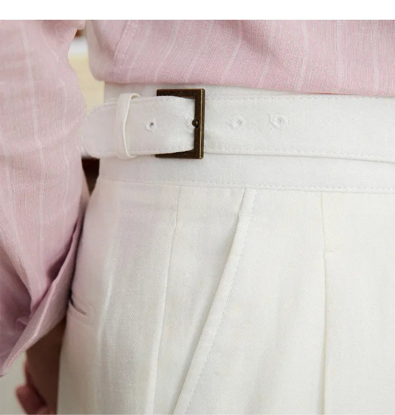 Pantalons en lin et coton à taille haute, coupe droite plissée, avec une ceinture en cuir blanc présentant une boucle en laiton et des détails de broderie discrets
