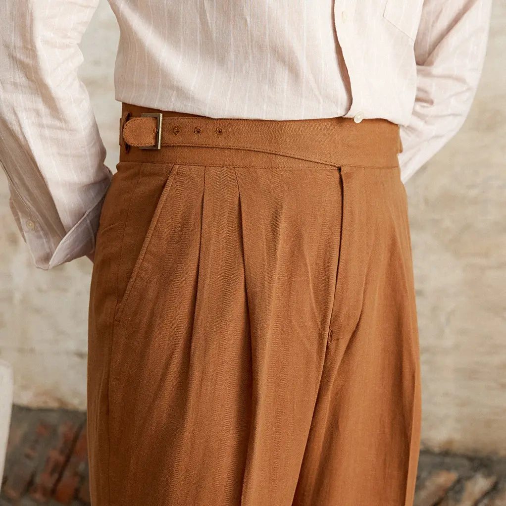 Pantalons beige camel en lin et coton à taille haute, coupe droite, avec des plis et un détail de taille ceinturée.