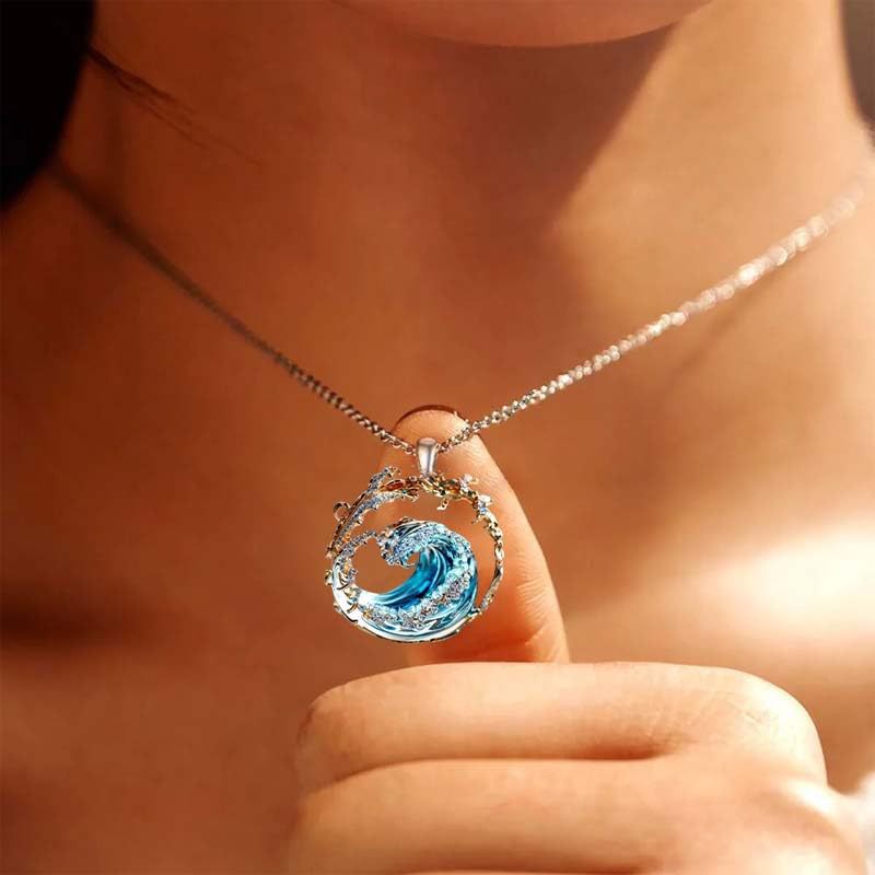 A delicate silver chain necklace features a circular ocean wave turquoise glass pendant with an intricate translucent blue design encased in clear resin with gold accents.
