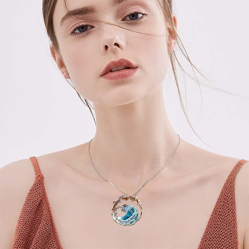 A delicate silver chain necklace features a circular ocean wave turquoise glass pendant encased in a textured gold-toned frame.