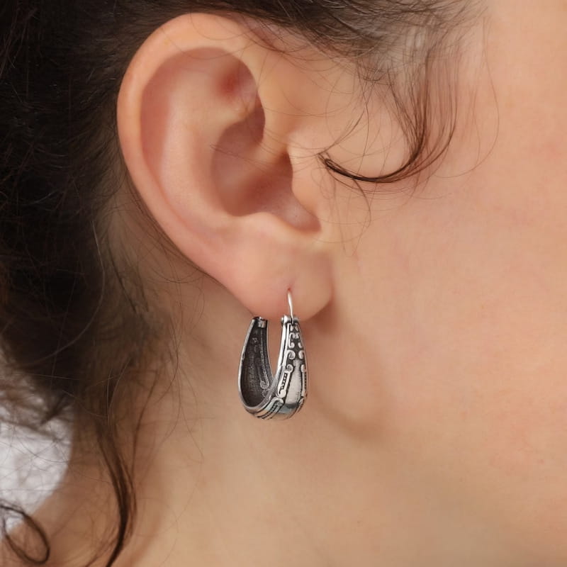 Boucle d’oreille créole vintage en alliage d’argent, teinte argent, avec des détails texturés complexes et une forme allongée légèrement courbée.
