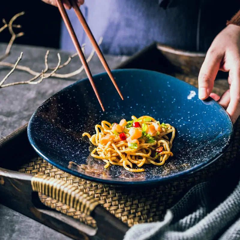 Deep blue speckled ceramic bowl holding a serving of noodles featured in the ceramic blue speckled Nordic round corner fillet plate collection.