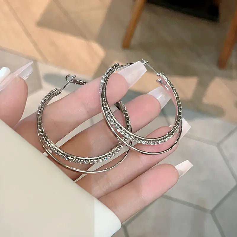 Silver hoop earrings with a double layered design featuring sparkling rhinestones along the outer edge from the double layered crystal pave hoop earrings collection.