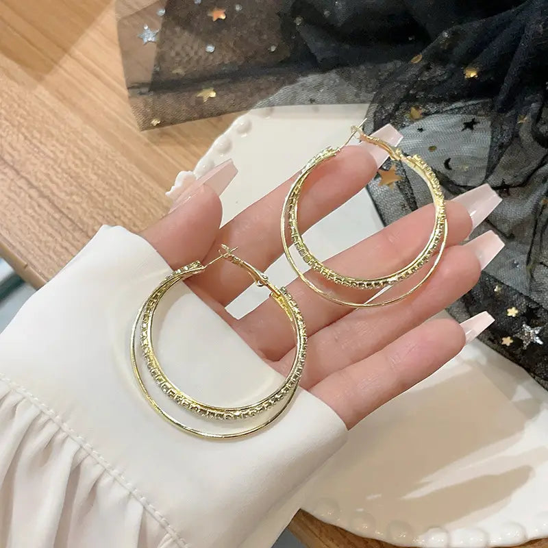 Gold-toned hoop earrings with a double-layer design and sparkling rhinestone accents featured in double layered crystal pave hoop earrings.