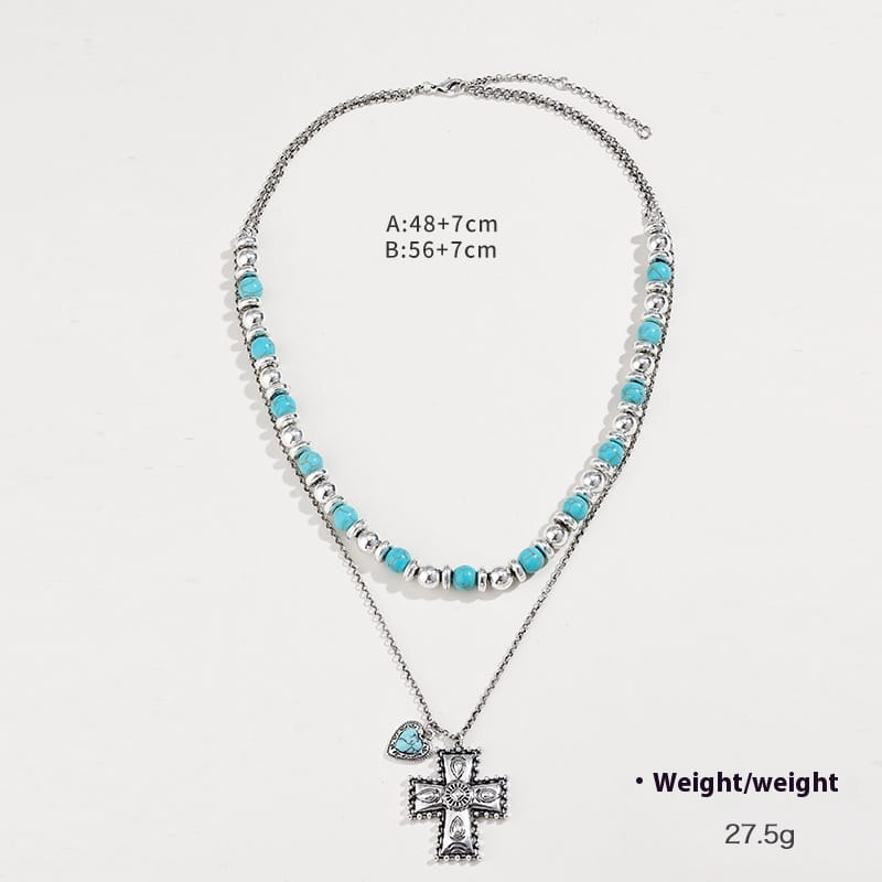 Silberfarbene Lagenhalskette mit türkisfarbenen Perlen, einem detaillierten Kreuzanhänger und passendem Herzanhänger aus dem Schmuckset „Turquoise Heart and Sunburst Silver Jewelry Set“.