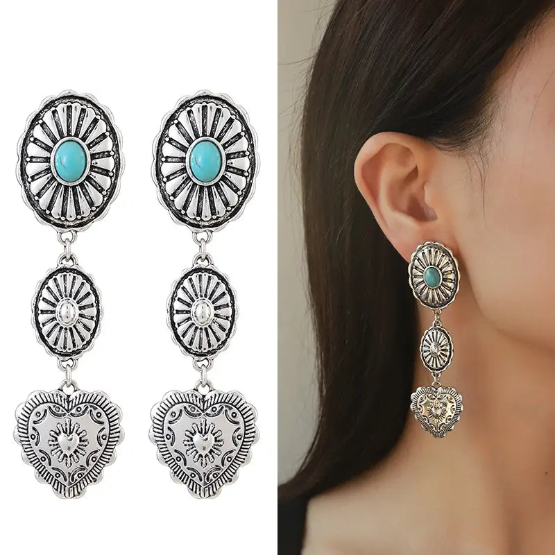 Silberfarbene Hängeohrringe aus dem Schmuckset „Turquoise Heart and Sunburst Silver Jewelry Set“ mit einem türkisfarbenen Stein, einem klaren Kristall-Ovalanhänger und einem detailliert gestalteten herzförmigen Anhänger.
