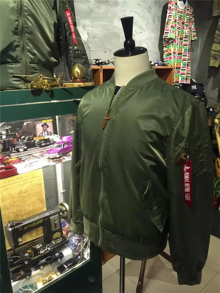 Olive green satin-finish Ma1 pilot bomber jacket with a casual stand collar and a red Alpha Industries logo tag on the left sleeve.