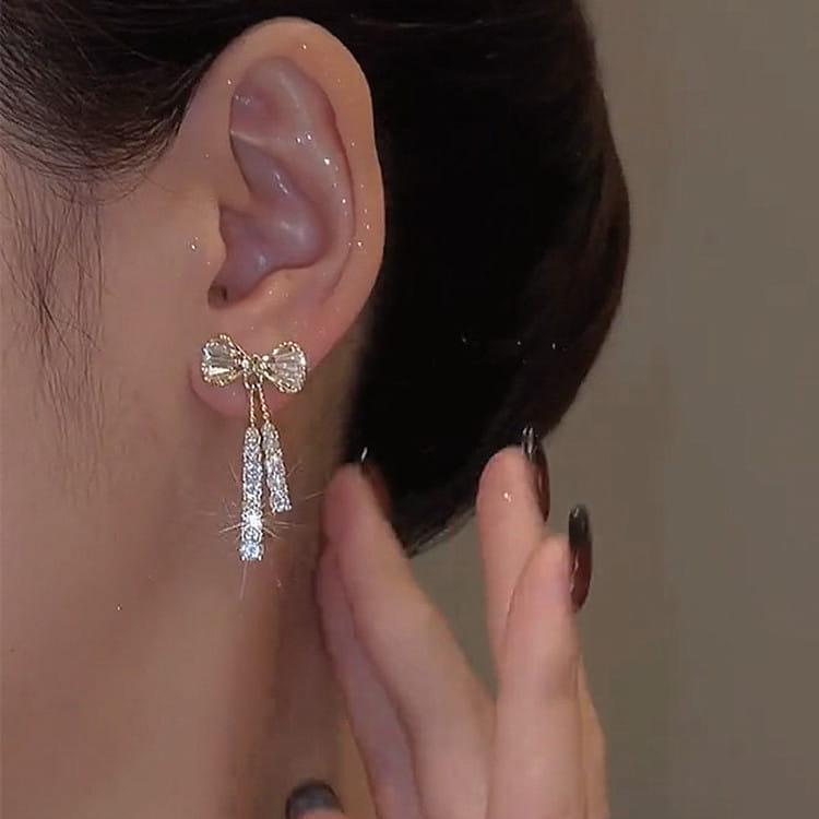 Crystal bow and pearl dangle earrings in gold featuring delicate gold-toned bow shapes adorned with sparkling clear crystals and dangling crystal strands.