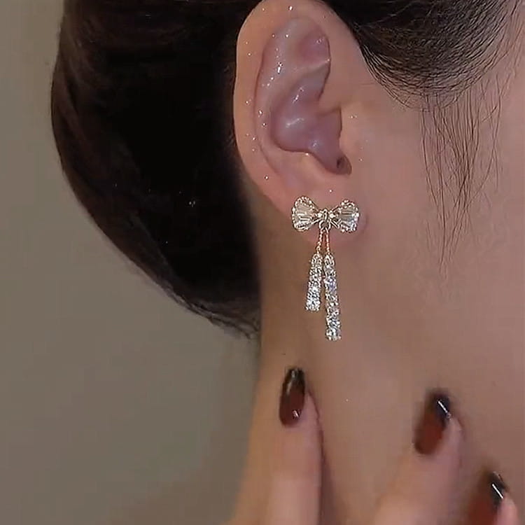 Crystal bow and pearl dangle earrings in gold featuring a delicate gold-toned bow adorned with sparkling clear crystals and dangling crystal strands.