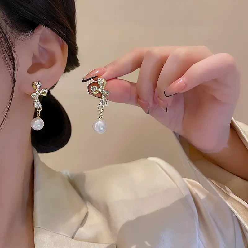 Crystal bow and pearl dangle earrings in gold featuring gold-toned cross shapes adorned with sparkling crystals and white pearl dangles.