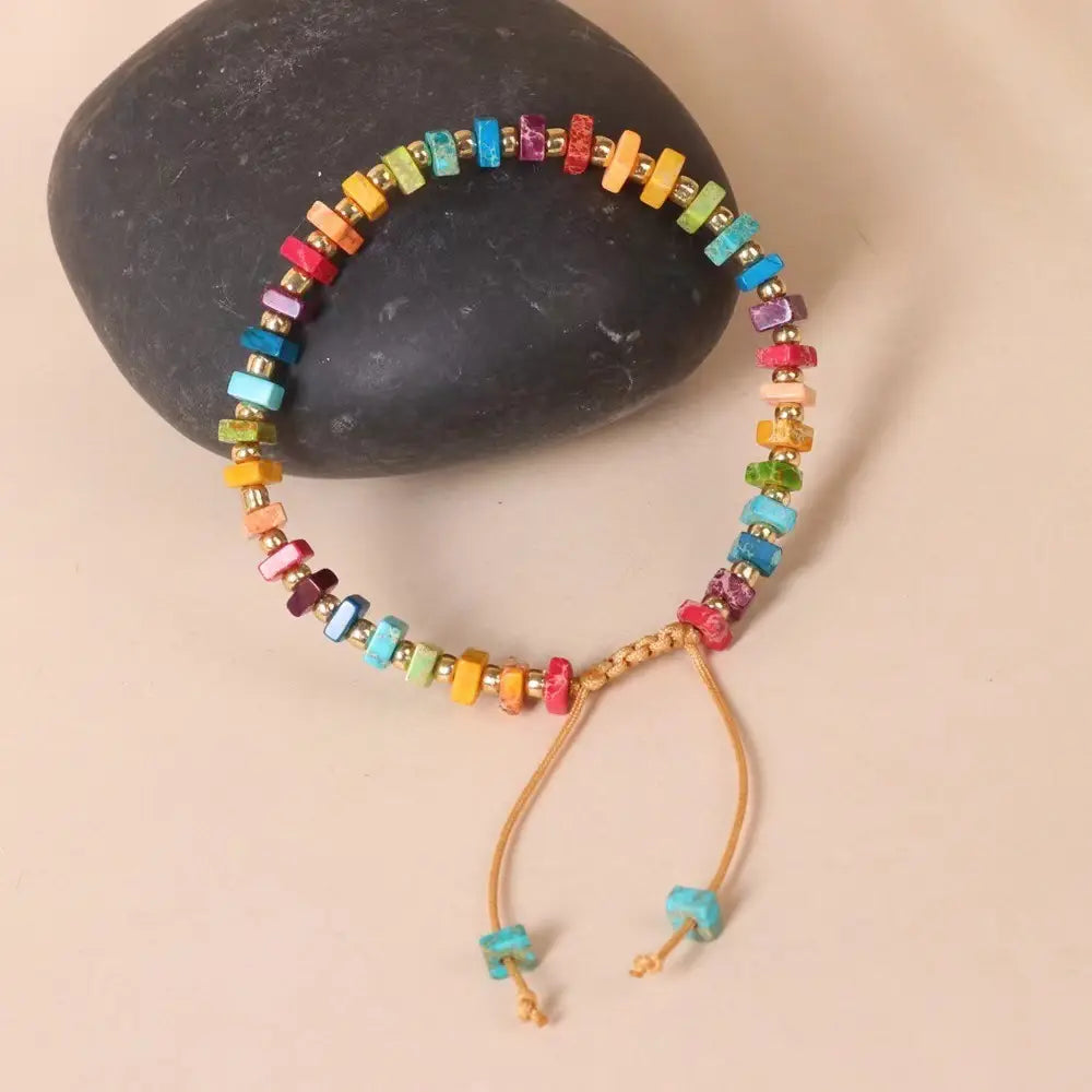 A handcrafted rainbow square stone woven yoga bracelet featuring rectangular multicolored stone beads strung on a light brown cord with adjustable ties.