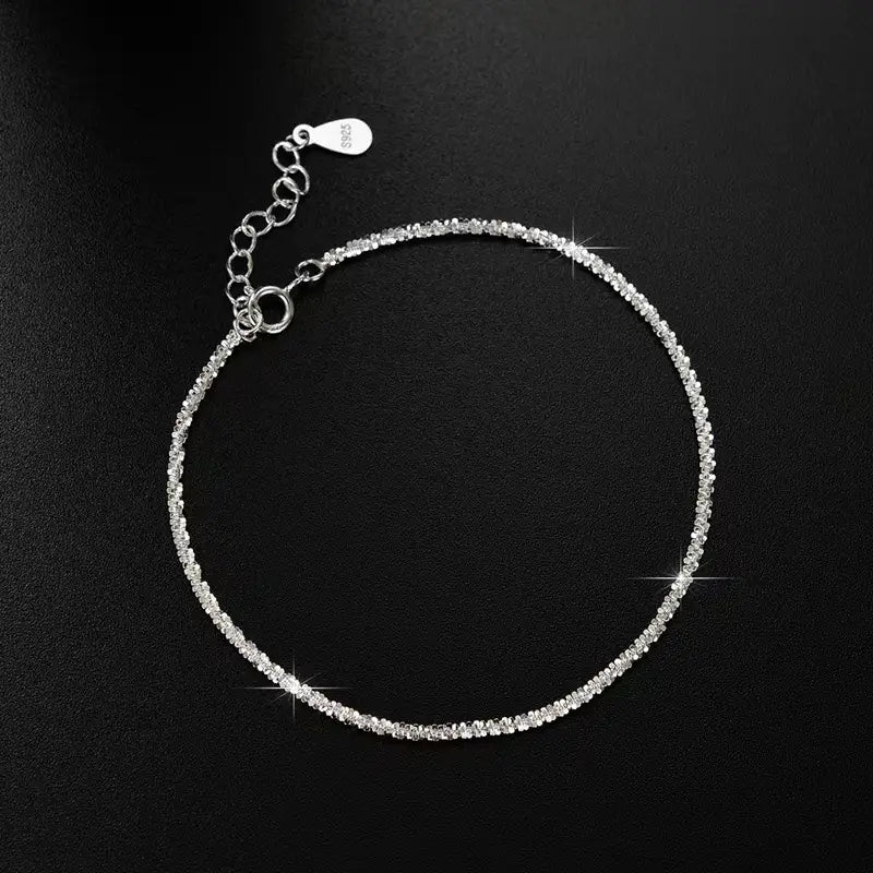 A delicate silver anklet adorned with a continuous line of sparkling clear crystals from an adjustable 925 silver sparkling crystal bracelet and anklet set.