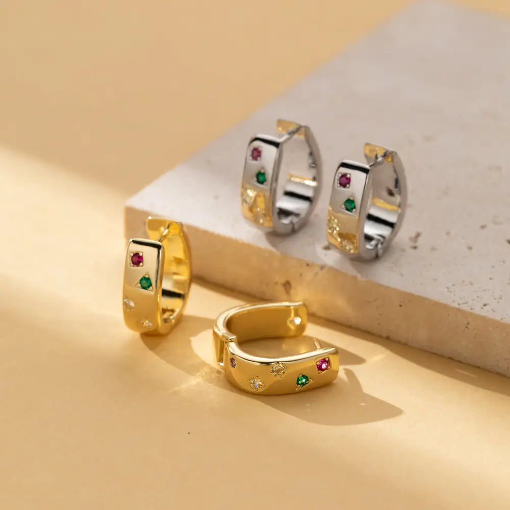 Gold-colored geometric multi color zircon huggie hoop earrings with embedded red green and clear gemstones.