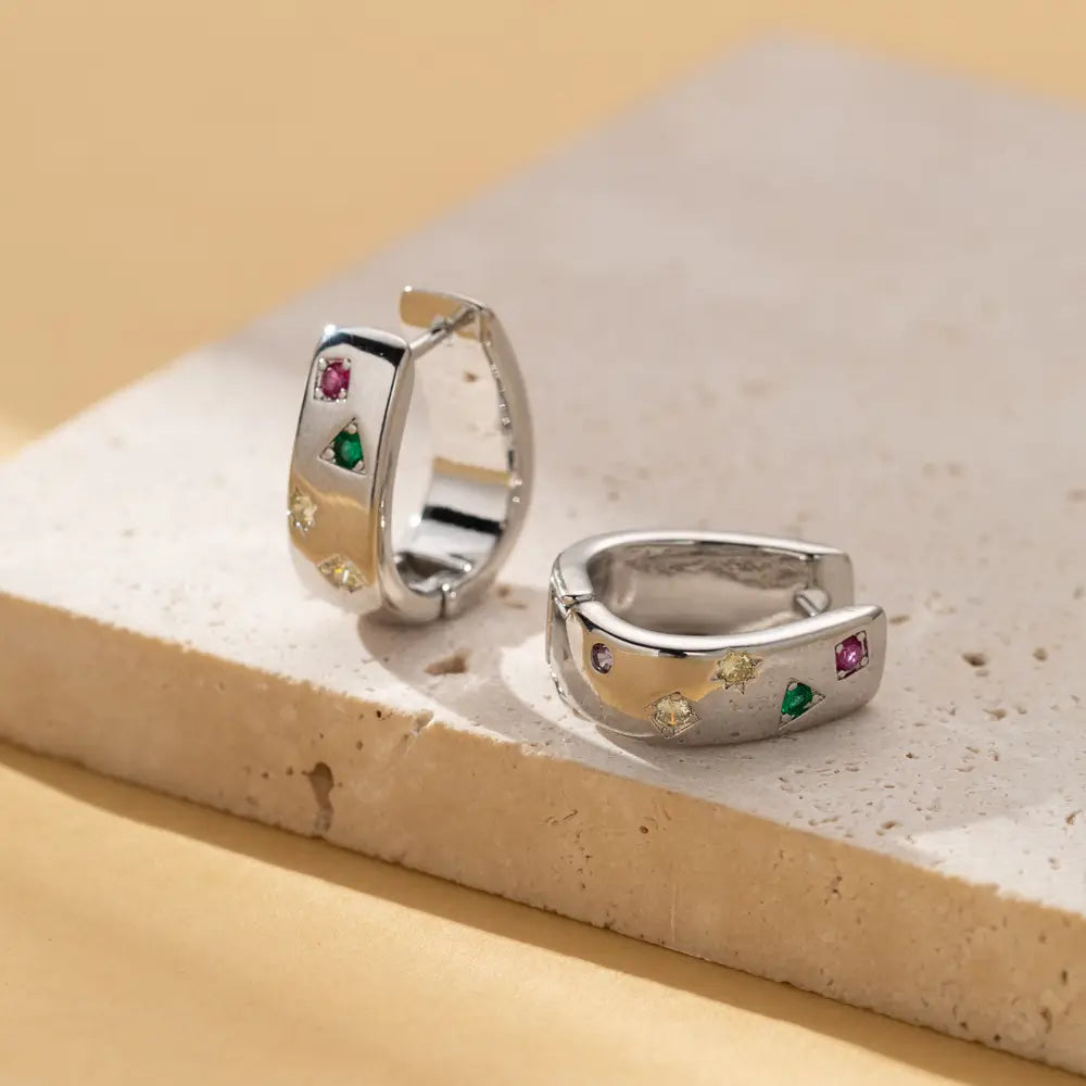 Silver hoop earrings featuring a geometric pattern adorned with multicolor zircon gemstones in a huggie style