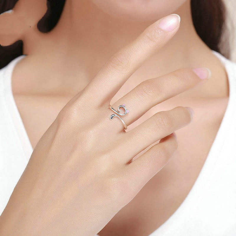 A delicate 925 sterling silver pink enamel cat ring with a minimalist open design featuring an elegant swirl and a small purple gemstone accent.