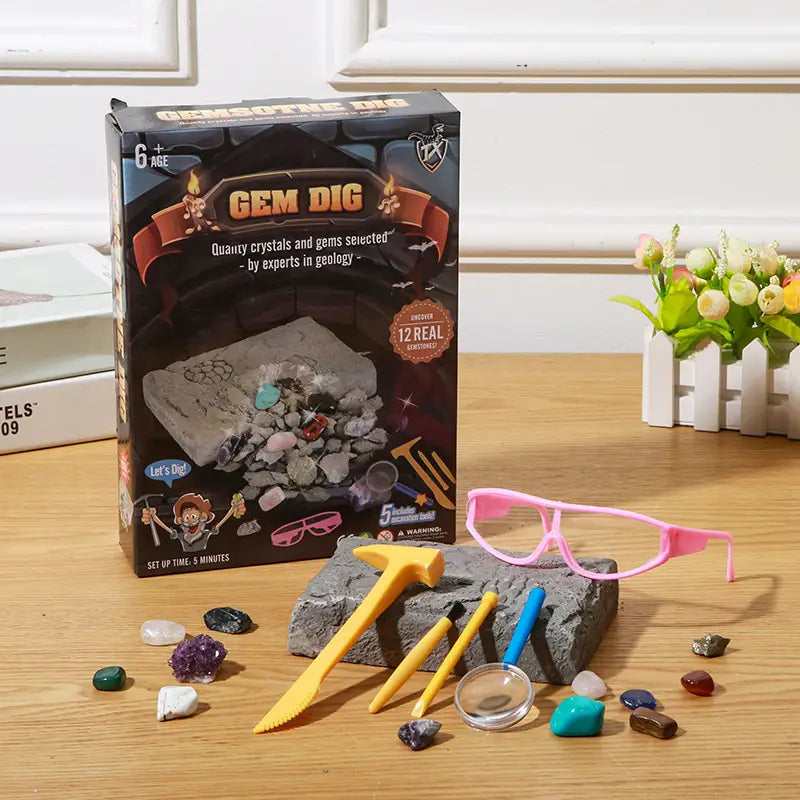 lunettes de protection à monture en plastique rose avec verre transparent posées sur une roche grise, à côté des outils du kit d’extraction de pierres précieuses pour enfants, jouet de géologie STEM.
