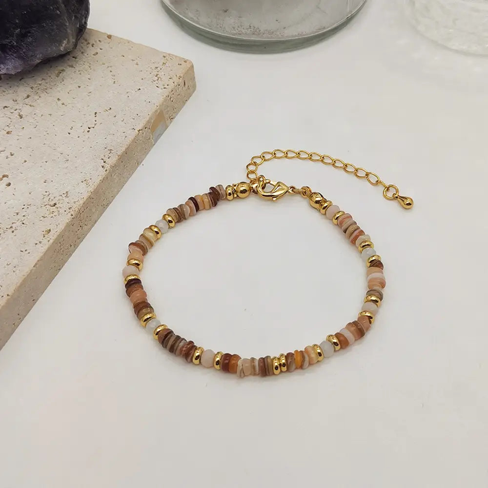 A handwoven rainbow shell beaded bracelet featuring a delicate gold-toned clasp and a mix of earthy brown tan and cream-colored stone beads with small metallic spacers.