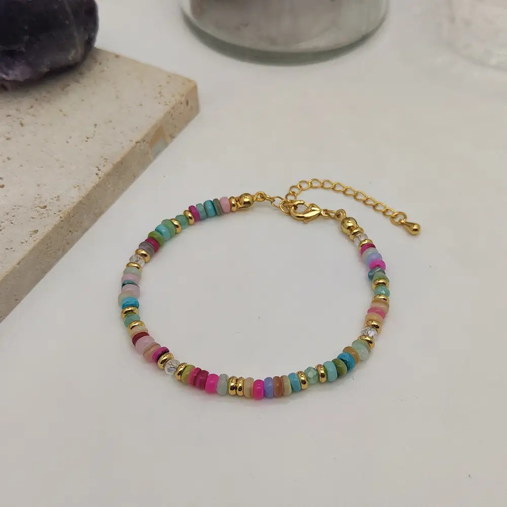 Handwoven rainbow shell beaded bracelet featuring colorful multicolored round beads in shades of pink teal turquoise lavender and peach with gold-toned metal accents and a gold clasp.
