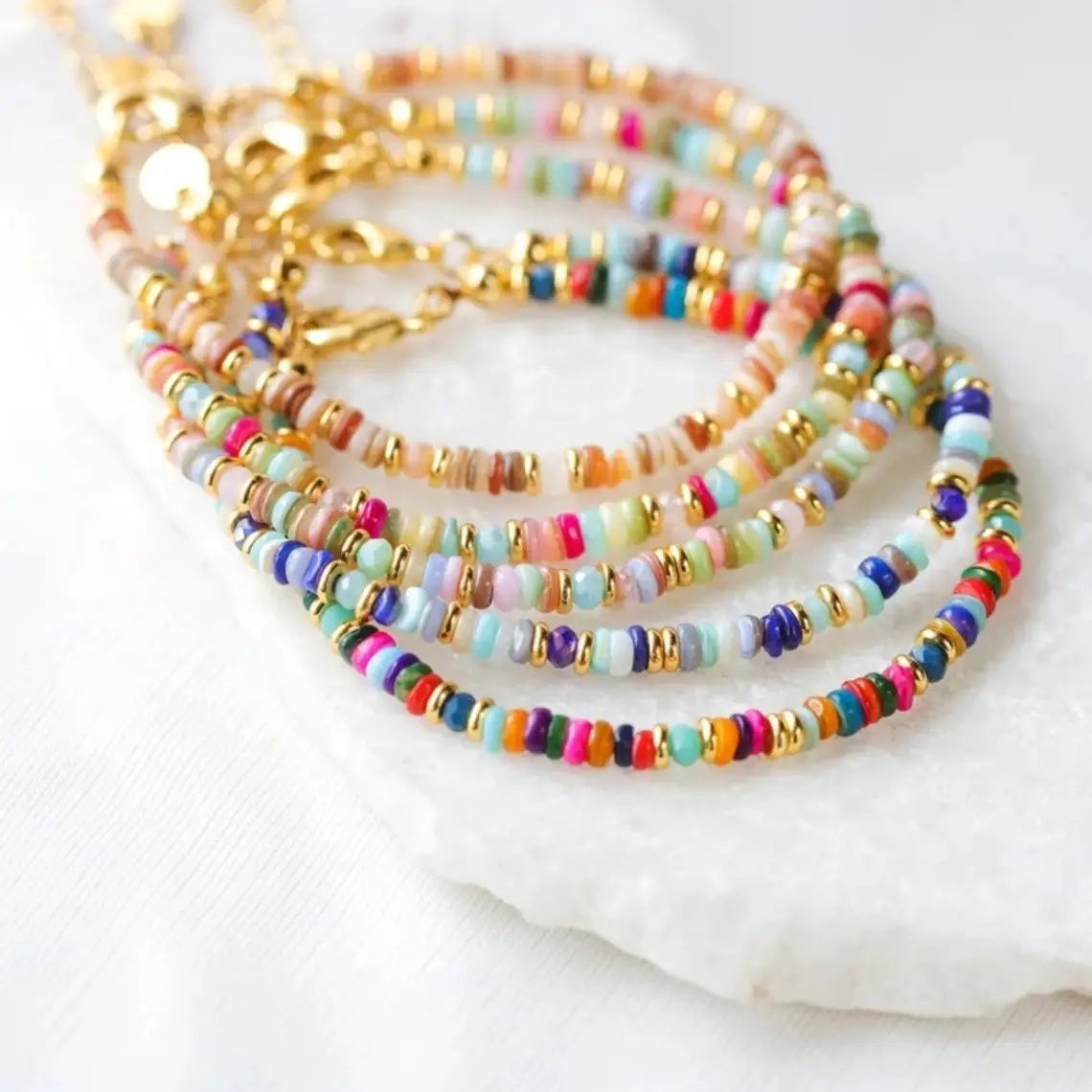A set of colorful handwoven rainbow shell beaded bracelets featuring multicolored cylindrical beads in pastel and vibrant hues with gold-toned clasps.