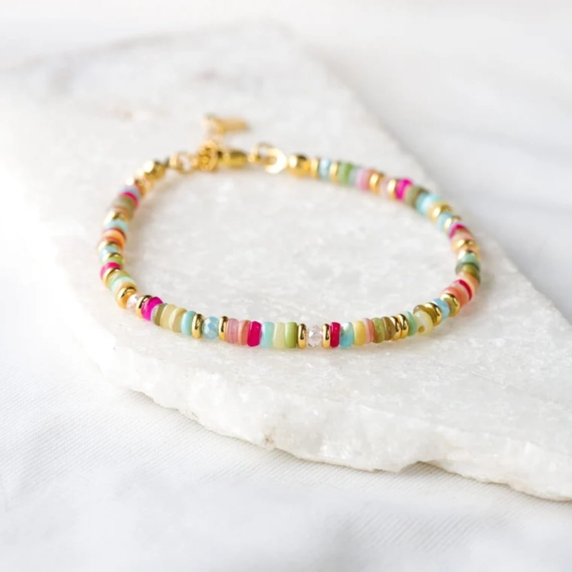 Handwoven rainbow shell beaded bracelet featuring a delicate mix of pastel and bright cylindrical beads with gold-toned spacers and a small gold clasp.