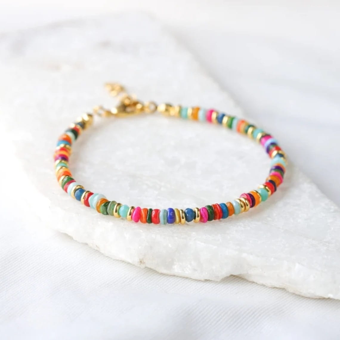 Handwoven rainbow shell beaded bracelet with a gold clasp featuring multicolored cylindrical beads in pink blue green orange and yellow.