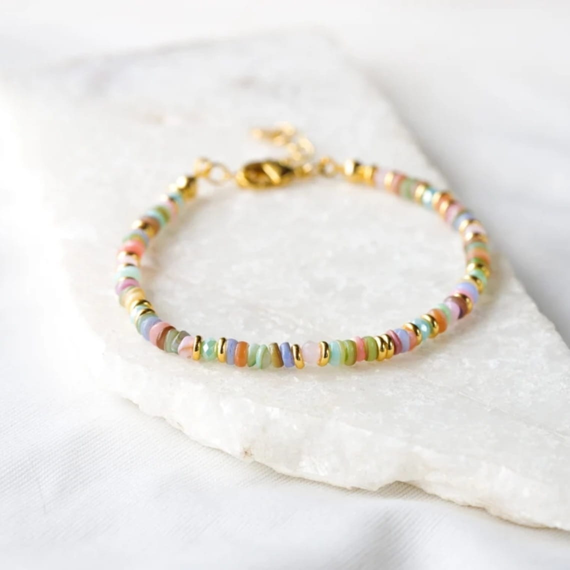 Handwoven rainbow shell beaded bracelet featuring pastel-colored beads with gold-toned metal clasp and accents.