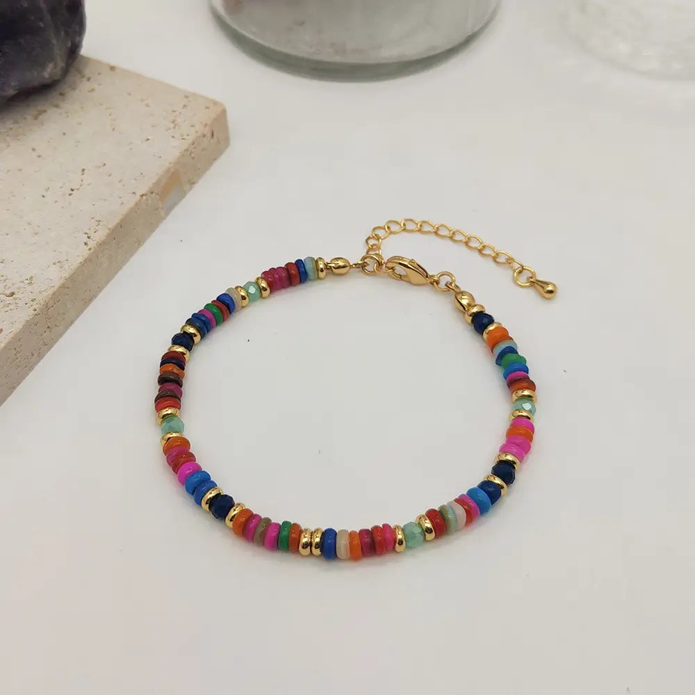 Handwoven rainbow shell beaded bracelet with a gold-toned clasp and chain featuring round beads in vibrant pink blue orange green red and black.