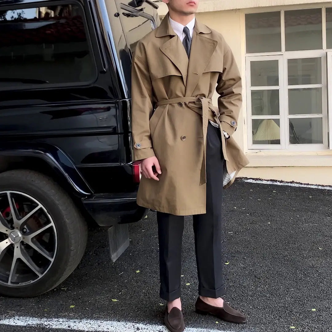 A tan double breasted trench coat for men with a belted waist and a classic tailored fit.