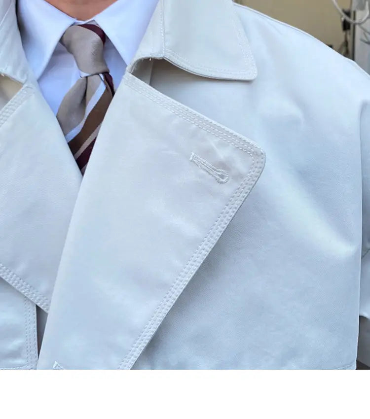 Double breasted trench coat for men in white with smooth slightly glossy fabric and neat stitching along the collar and lapel.