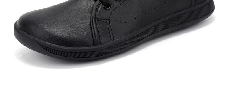 Zapatilla minimalista antideslizante de cuero negro de puntera ancha con perforaciones sutiles a lo largo del lateral.