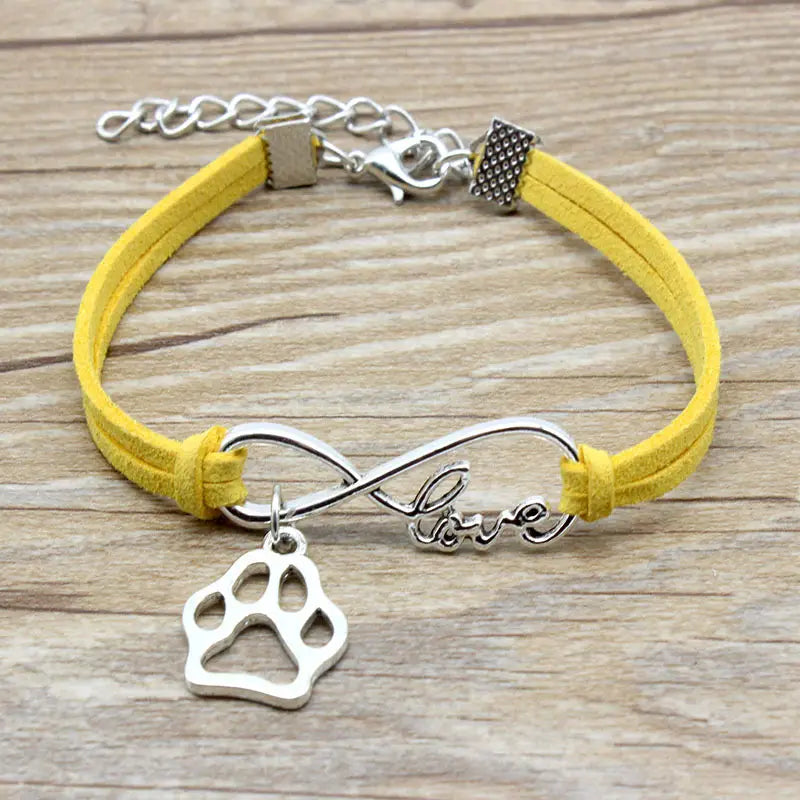 Yellow suede hand-woven bracelet featuring a silver infinity charm engraved with love and a dangling paw print pendant.