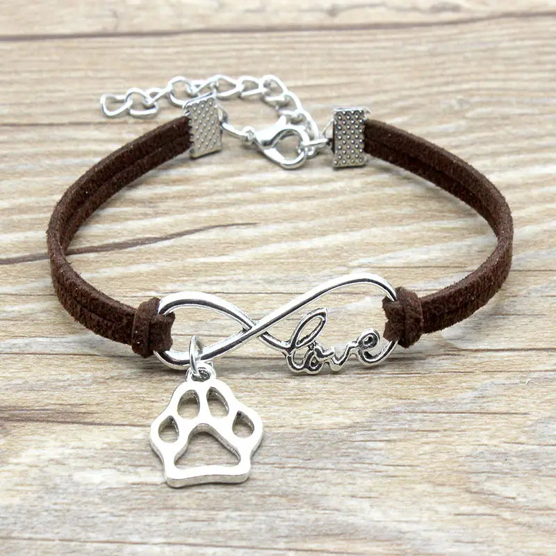 Brown suede hand-woven infinite love bracelet featuring a silver infinity charm engraved with love and a dangling paw print pendant.