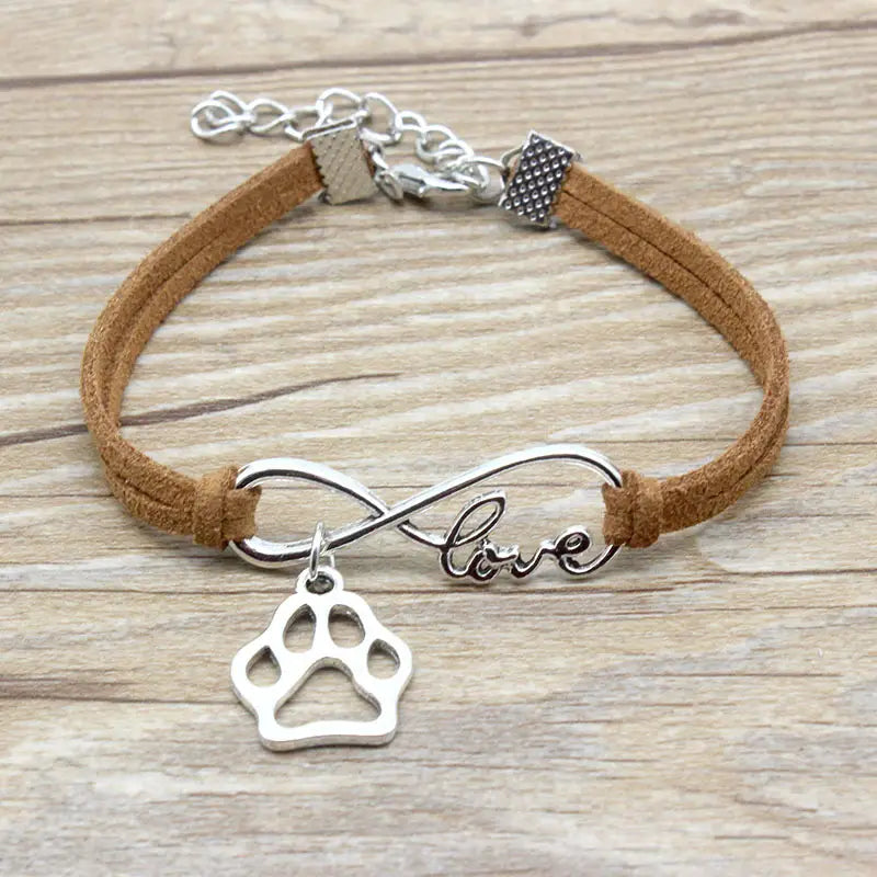 A hand-woven infinite love pet paw suede bracelet featuring a silver infinity charm with a paw print pendant and the word love engraved on its band with tan suede cord.