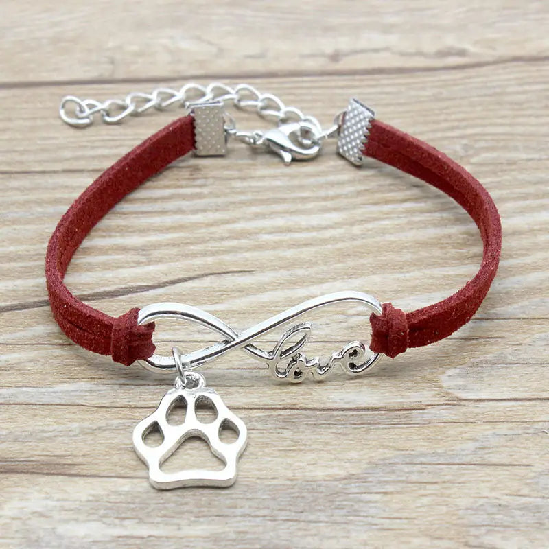 Red suede bracelet featuring a silver infinity symbol charm engraved with love and a dangling paw print pendant for pet lovers.