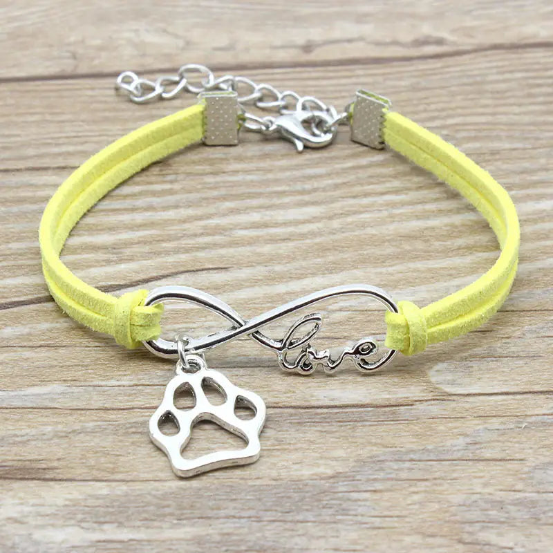 A delicate yellow suede hand-woven bracelet featuring a silver infinity symbol charm engraved with love and a matching paw print pendant.