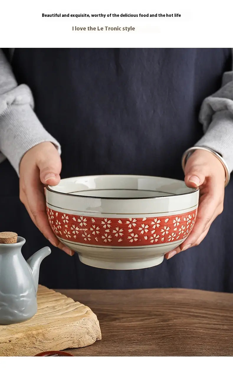 A white ceramic 7 inch noodle bowl with a red band featuring delicate white floral patterns and black trim along the rim designed for serving soup.
