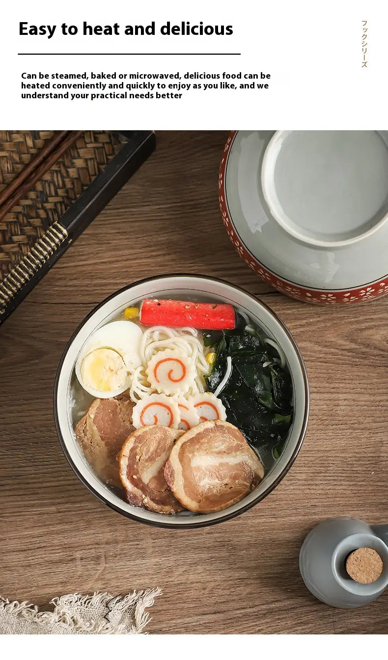 A ceramic noodle bowl with a white interior and dark rim filled with steaming ramen topped with sliced pork boiled egg seaweed noodles and carrot slices.