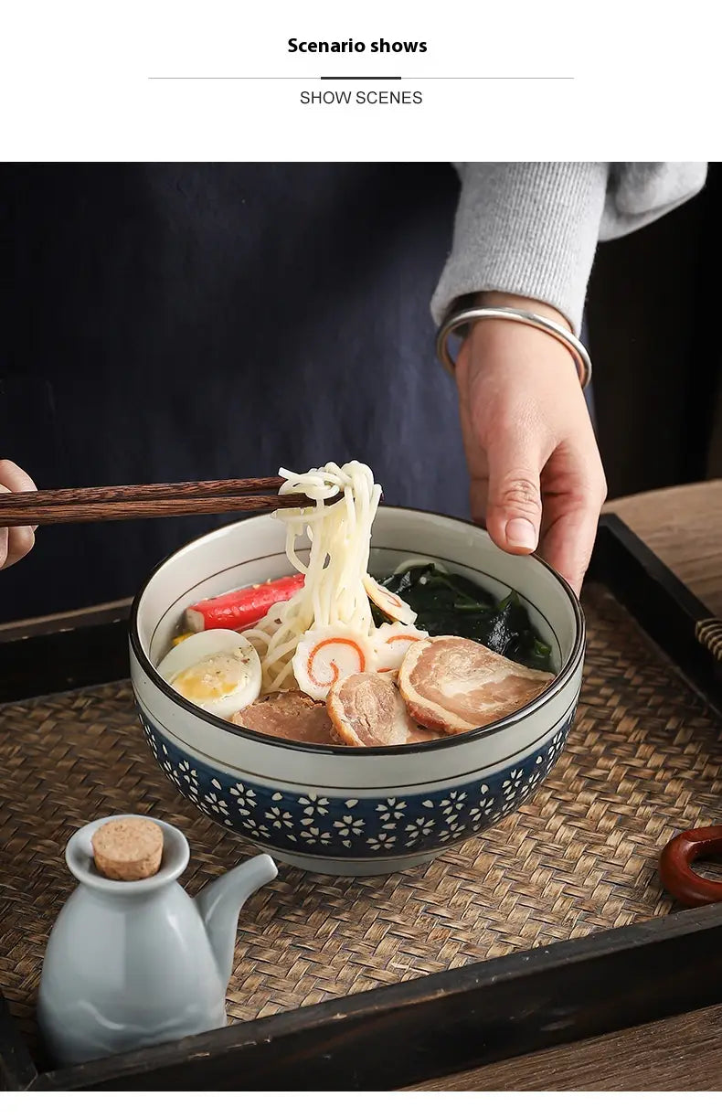 A ceramic noodle bowl with a blue and white floral cherry blossom pattern filled with noodles and toppings.