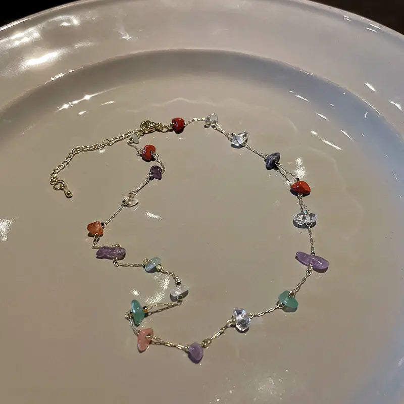 A multicolor gemstone choker in gold and silver alloy featuring a delicate silver chain necklace adorned with colorful irregularly shaped gemstone beads in red purple green and clear.