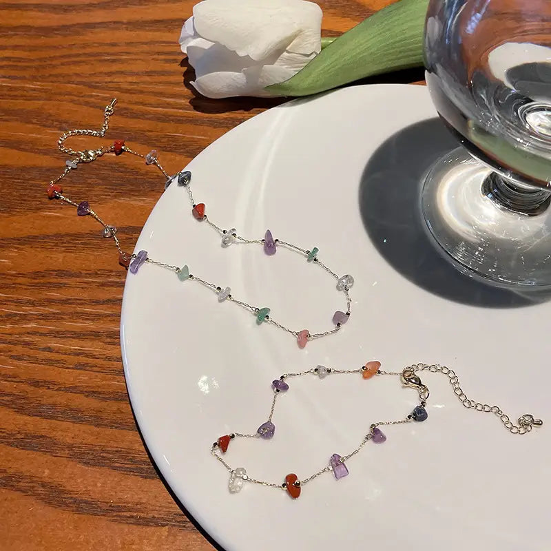 A delicate multicolor gemstone choker in gold and silver alloy featuring a silver chain with irregularly shaped red purple green orange and clear stones.