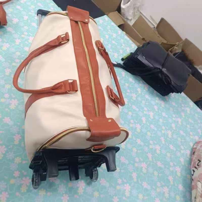 cream-colored rolling travel bag with tan leather straps and gold-toned zippers featuring a retractable handle system designed as a foldable large capacity fitness duffel.
