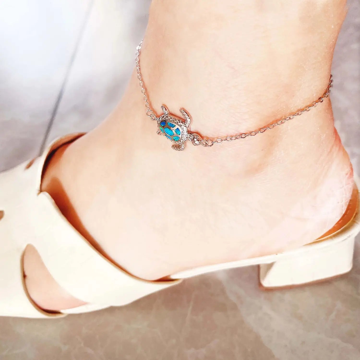 A delicate silver-toned anklet featuring a small intricately detailed sea turtle charm with vibrant turquoise opal inlay.