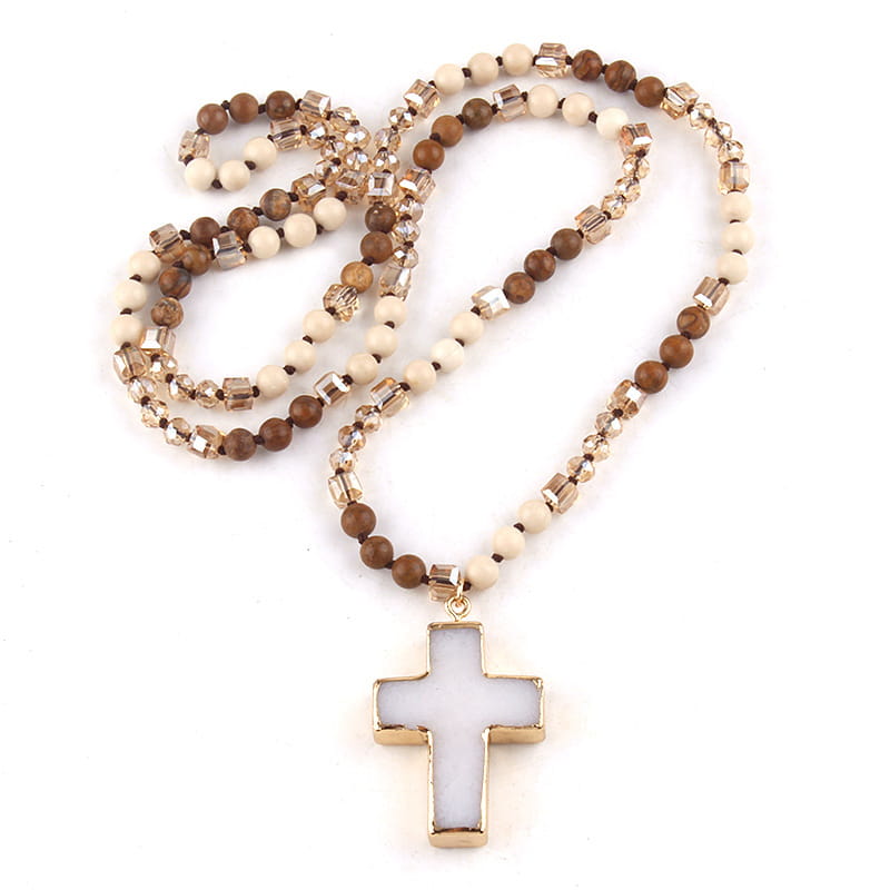 A gold-toned cross pendant with a white matte-finished center hanging from a beaded necklace featuring alternating brown wooden and cream-colored beads with clear crystal accents in a Bohemian natural stone and glass beaded cross necklace.