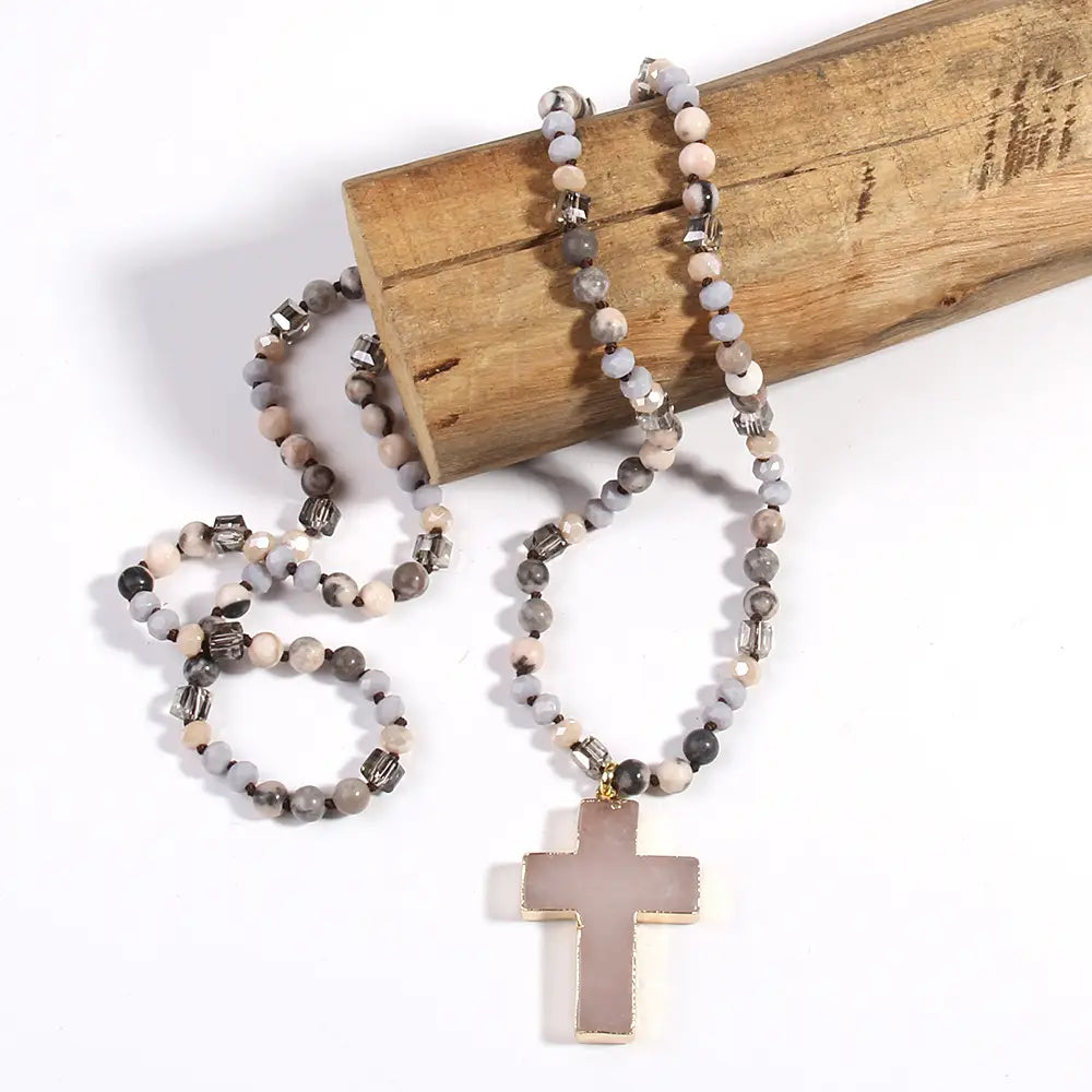 A delicate bohemian natural stone and glass beaded necklace featuring gray and beige stones with metallic accents and a matte finished cross pendant.