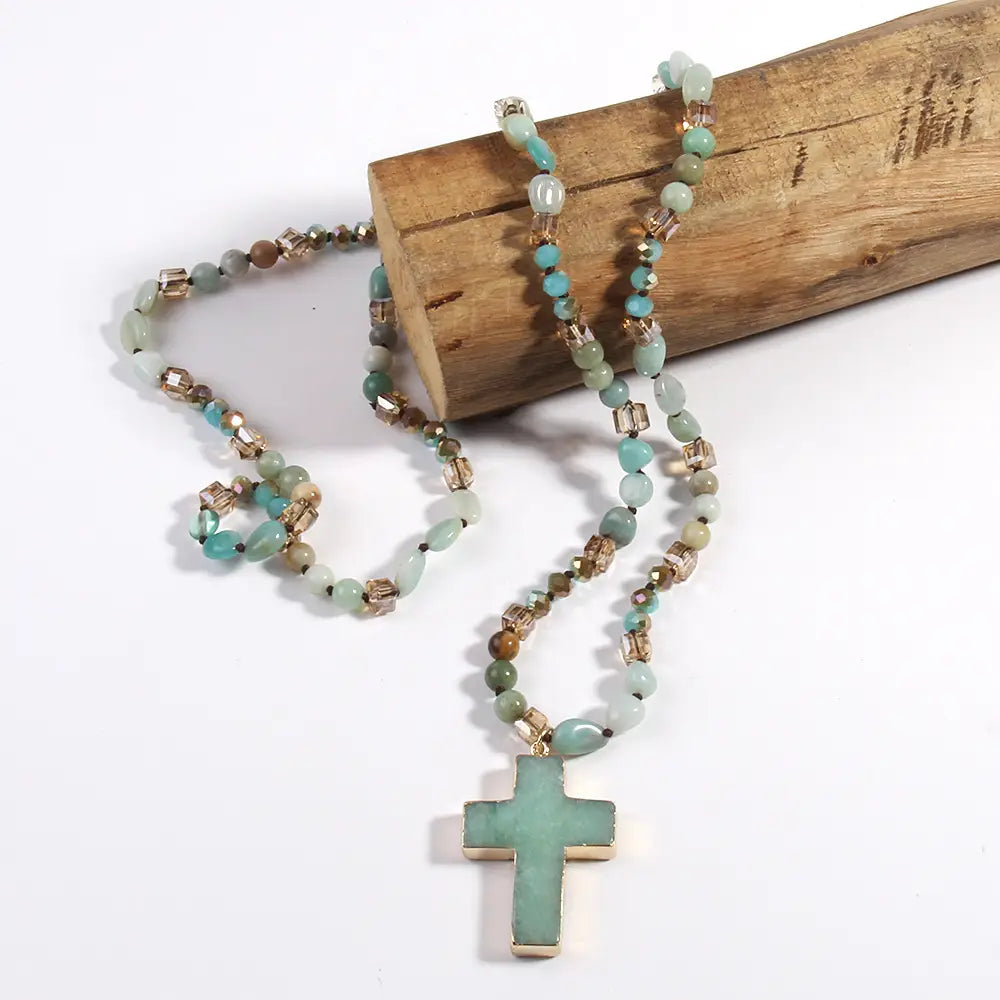 A delicate turquoise cross pendant necklace featuring jade-like beads and metallic accents from the bohemian natural stone and glass beaded collection.